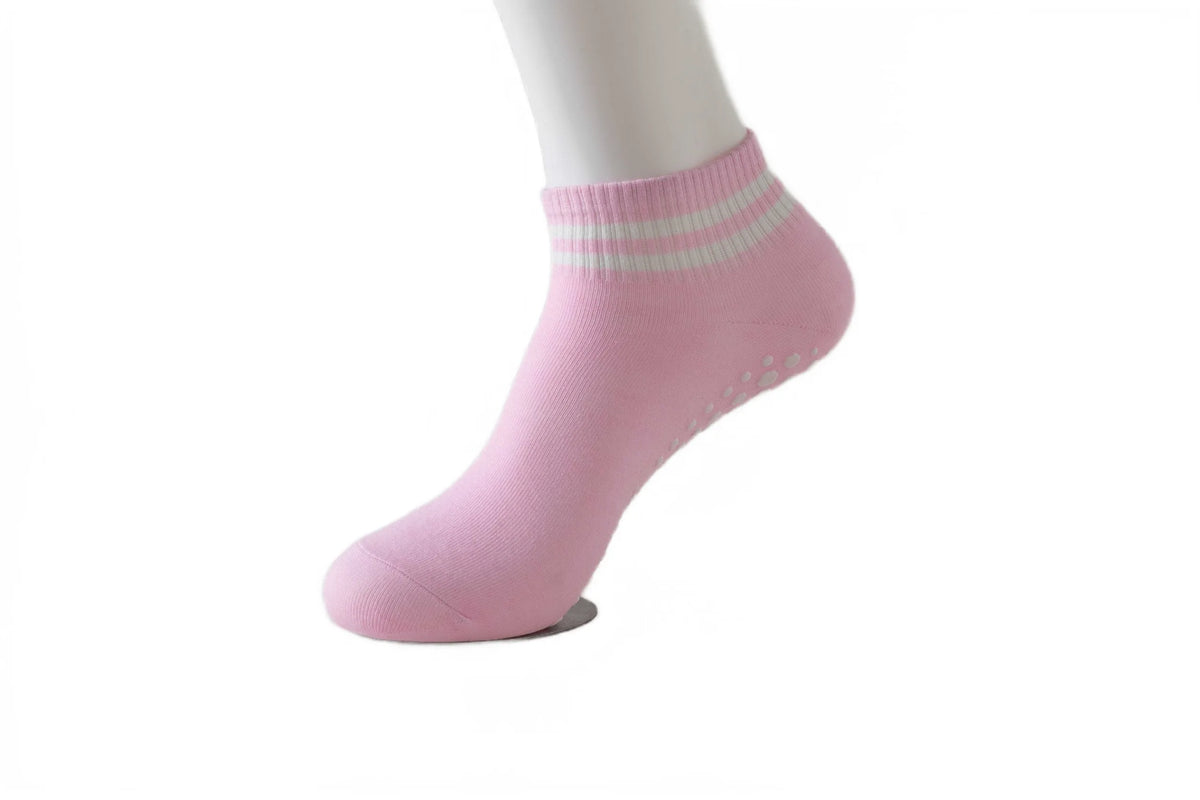 Pink non-slip grip socks with light green stripes worn on a white model's foot.