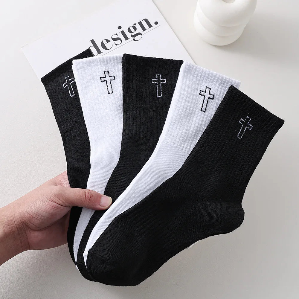A hand holds a stack of black and white men's high-cut breathable casual crew socks with crosses embroidered on them.