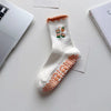 Chaussettes de yoga blanches avec broderie orange et détails antidérapants, posées sur une surface blanche.