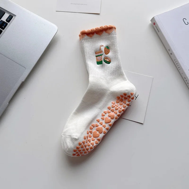 Chaussettes de yoga blanches avec broderie orange et détails antidérapants, posées sur une surface blanche.