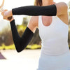 A woman wearing black arm sleeves and a white top is performing an exercise outdoors.