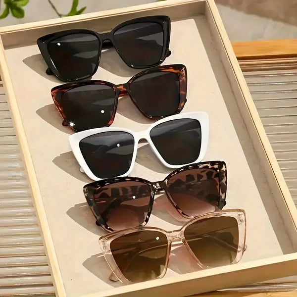 A collection of five cat eye vintage sunglasses in various shades and frames displayed in a light wooden tray.