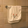 A white face towel with a cute rabbit design hangs on a metal rack against a tiled wall.