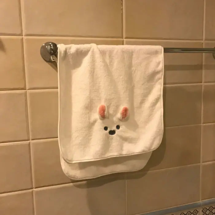 A white face towel with a cute rabbit design hangs on a metal rack against a tiled wall.