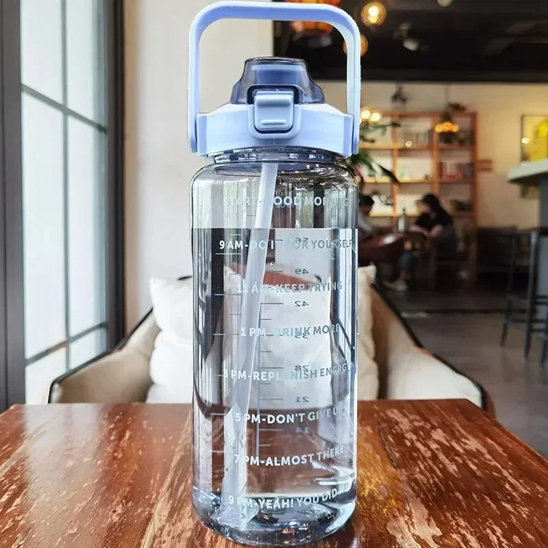 A clear insulated water bottle with a blue cap and straw is shown on a wooden table.