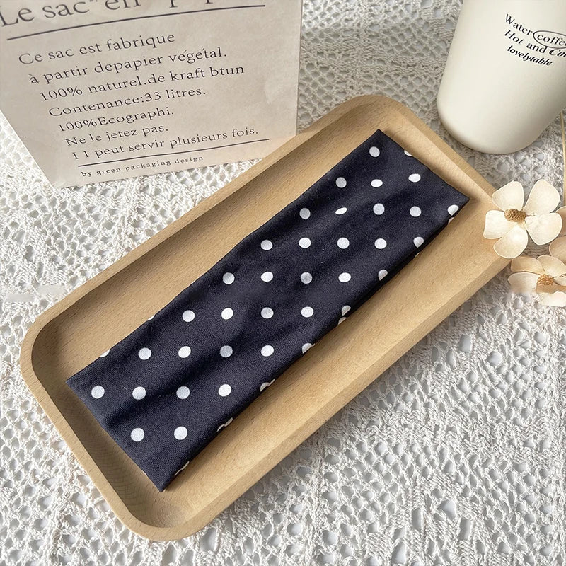 Dunkelblaue Polka-Dot-Haarband zeigt auf einem Holztablett neben einer Informationskarte.