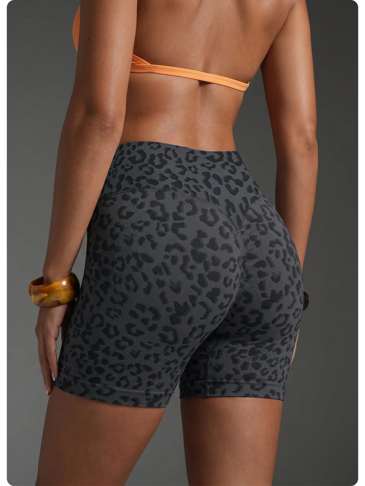 Une femme portant des shorts de yoga taille haute à imprimé léopard et un haut orange, vue de dos.