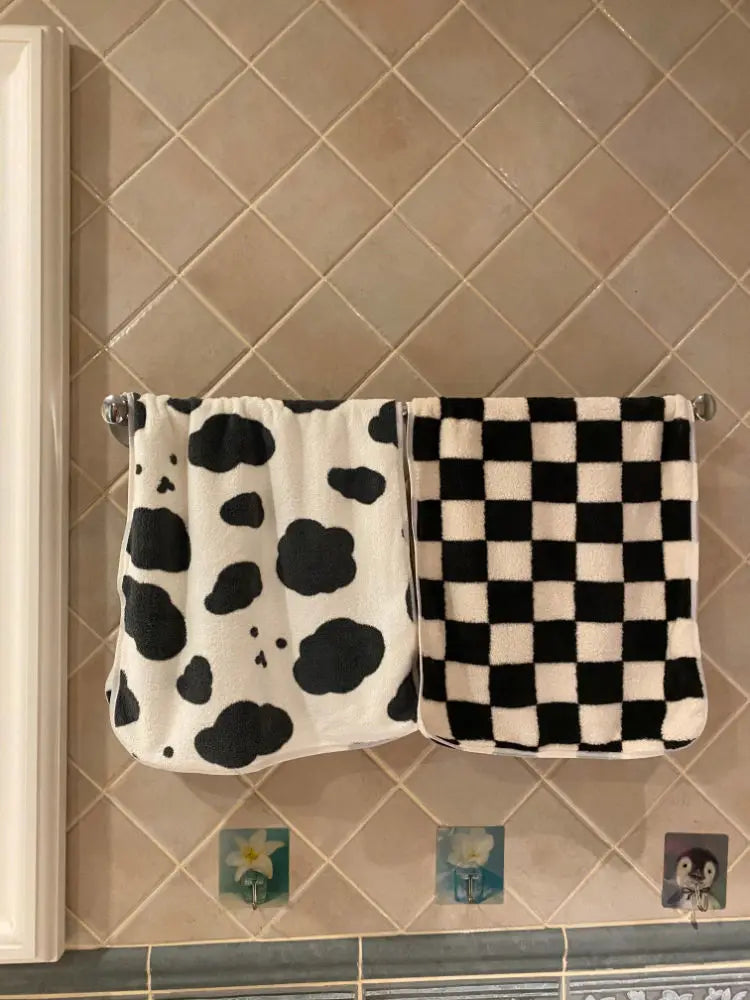 A pair of black and white patterned soft coral fleece face towels hanging on a tiled wall.
