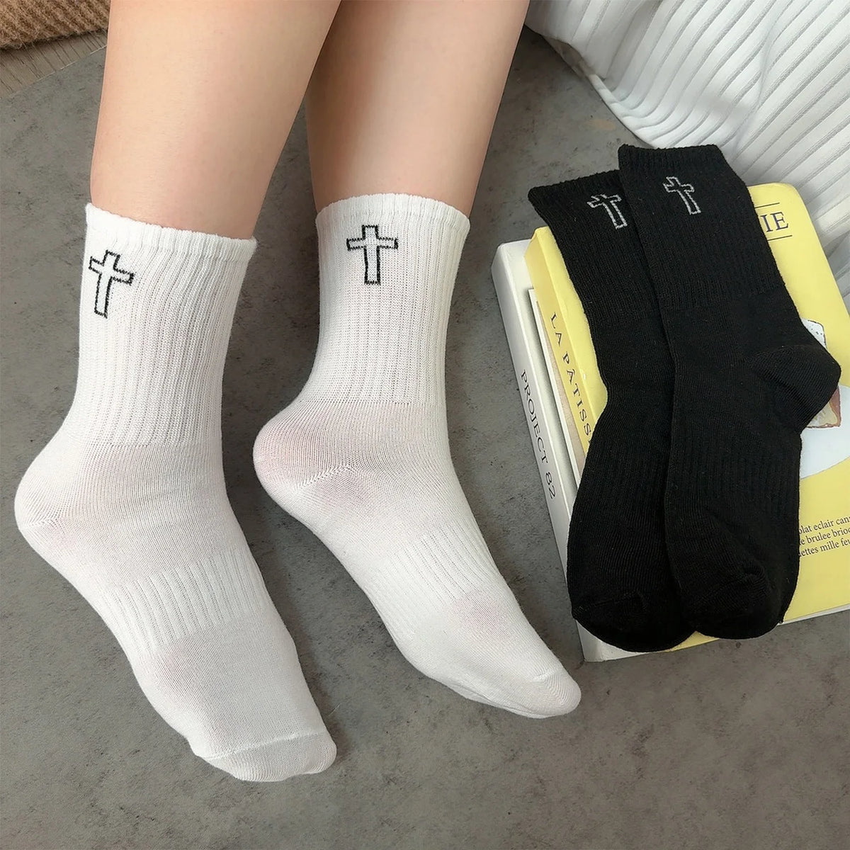 A pair of white and black high-cut breathable casual crew socks are displayed next to a yellow book.