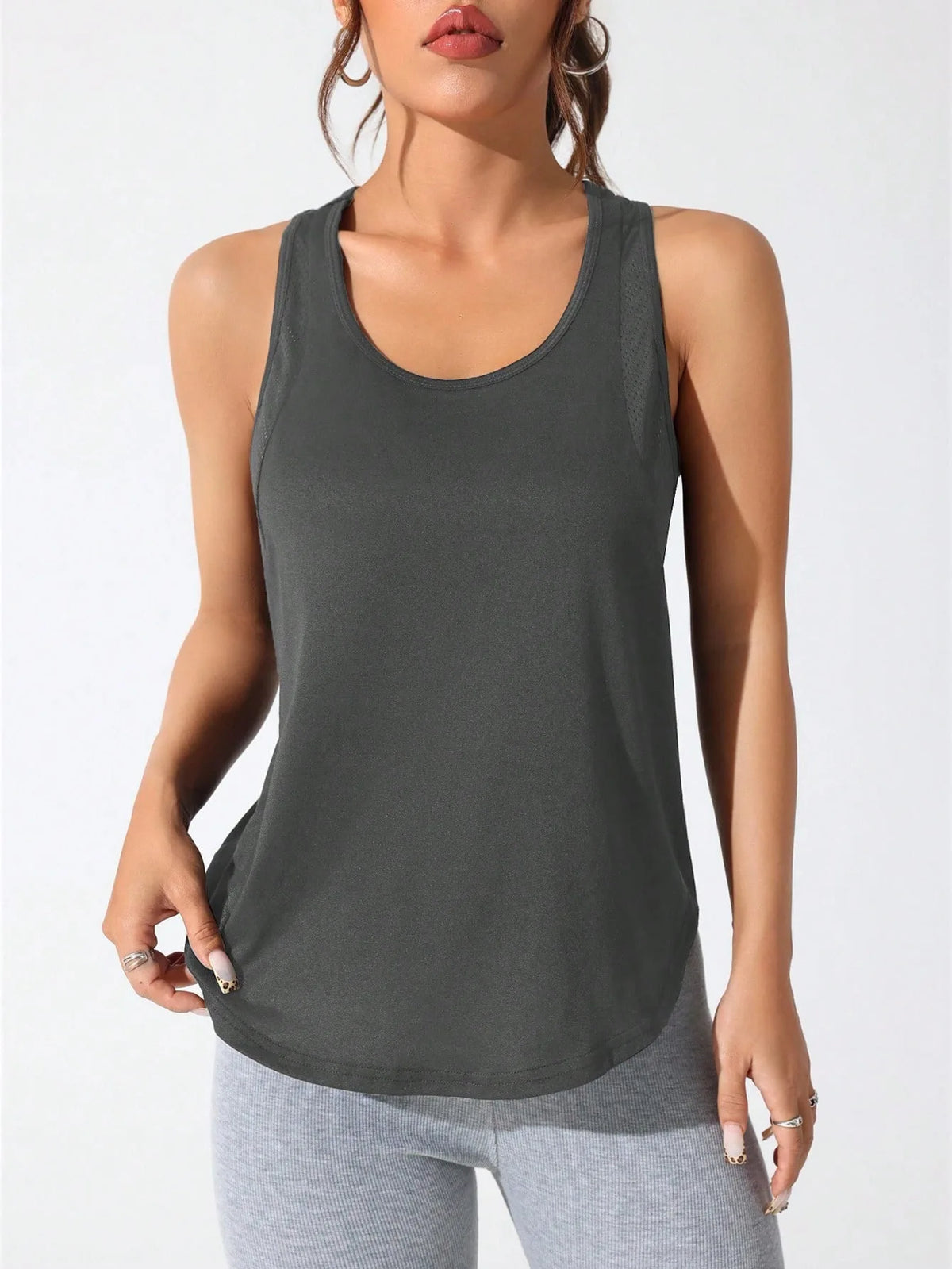 A woman wearing a dark gray running and yoga vest and light gray leggings.