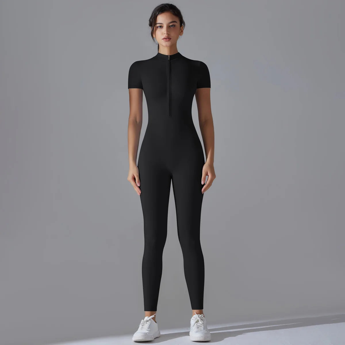 A model wearing a black Naked Zipper Yoga Jumpsuit standing against a gray background.