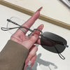 A hand holds a pair of black frameless rectangle blue light blocking glasses against a white background.