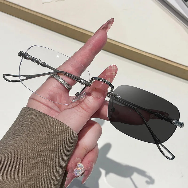 A hand holds a pair of black frameless rectangle blue light blocking glasses against a white background.