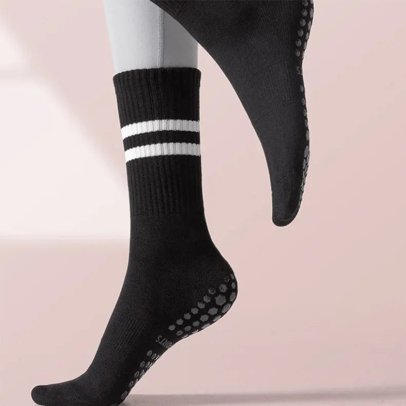 Black non-slip yoga socks with white stripes and dotted grip on a person's foot.