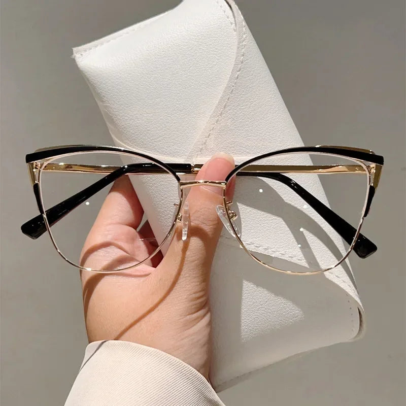A pair of black and gold cat-eye blue light blocking glasses are held against a white leather case.