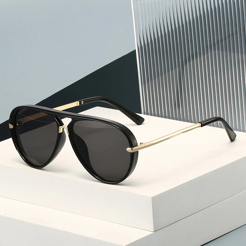 A pair of black retro pilot sunglasses with gold accents resting on a white surface.