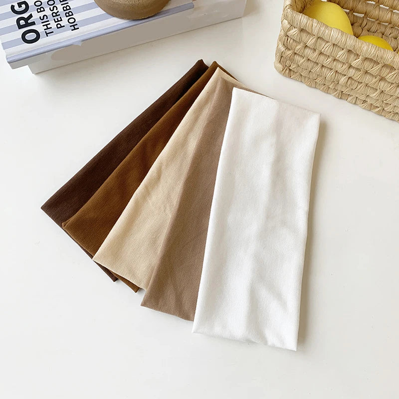 A stack of five brown, beige, and white elastic hairbands for fitness and yoga placed next to a book.
