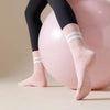 Pink yoga socks with white stripes worn by a person next to a large pink exercise ball.