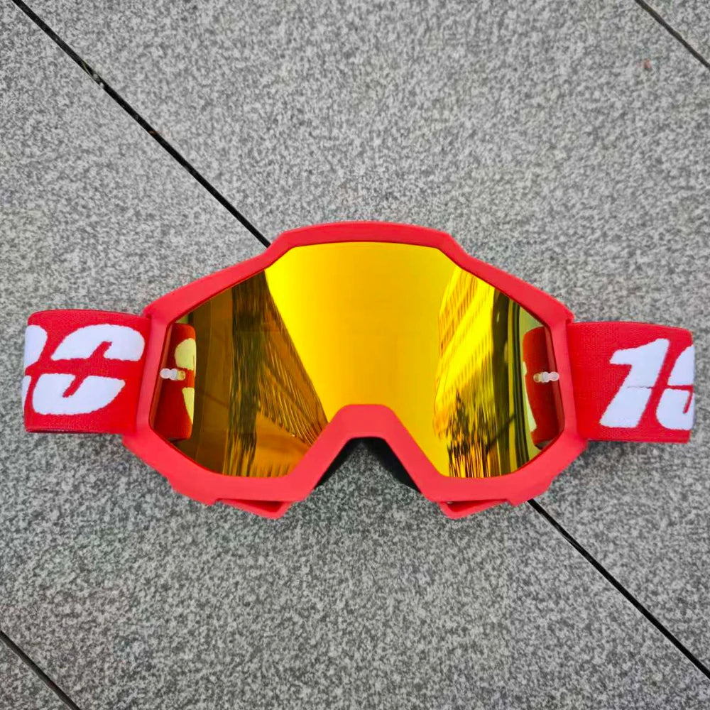 Une paire de lunettes de moto tout-terrain rouge vif avec des verres miroirs jaunes posées sur une surface grise.