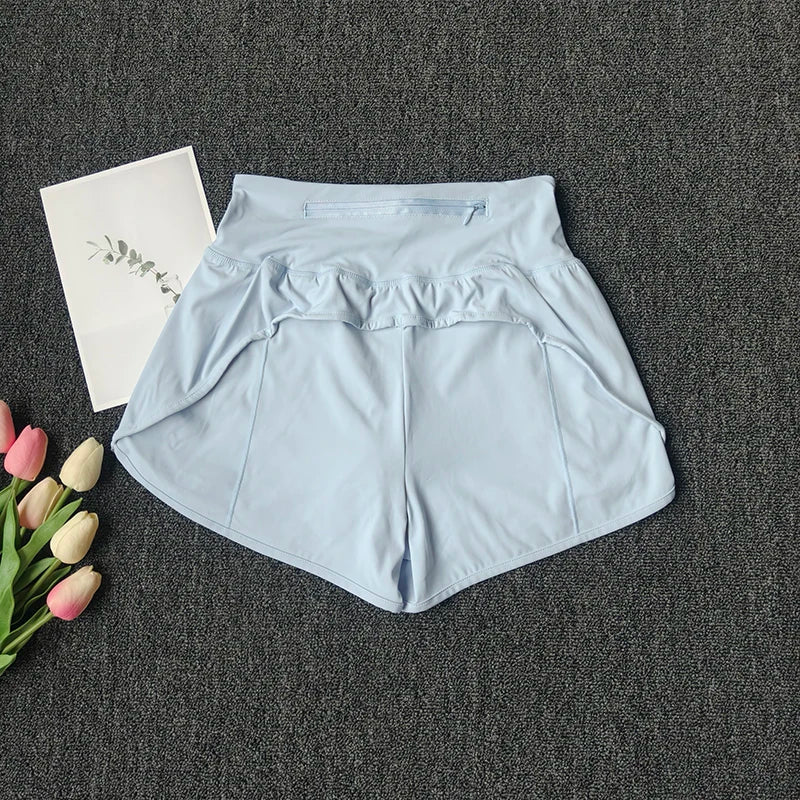 Light blue women's high-waist yoga and fitness shorts laid flat on a dark gray surface next to pink and white flowers.