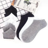 Una colección de calcetines de tobillo negros, blancos y grises junto a un folleto de descuento.