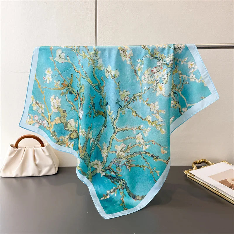 A turquoise silk-touch floral hair scarf with light green and white blossoms draped on a gray surface.