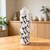 A white reusable water bottle with a black bow pattern sits on a wooden table.