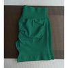 Un short de yoga sans couture, vert foncé et taille haute, est posé à plat sur une surface marron texturée.