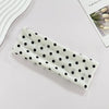 Un bandeau de yoga élastique blanc à pois noirs posé sur une surface claire.