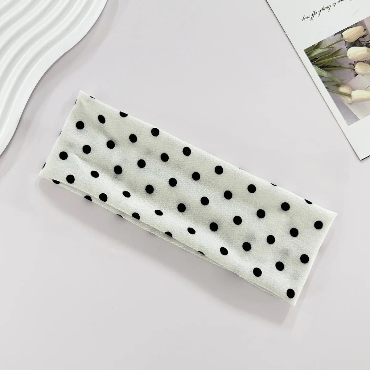 Un bandeau de yoga élastique blanc à pois noirs posé sur une surface claire.