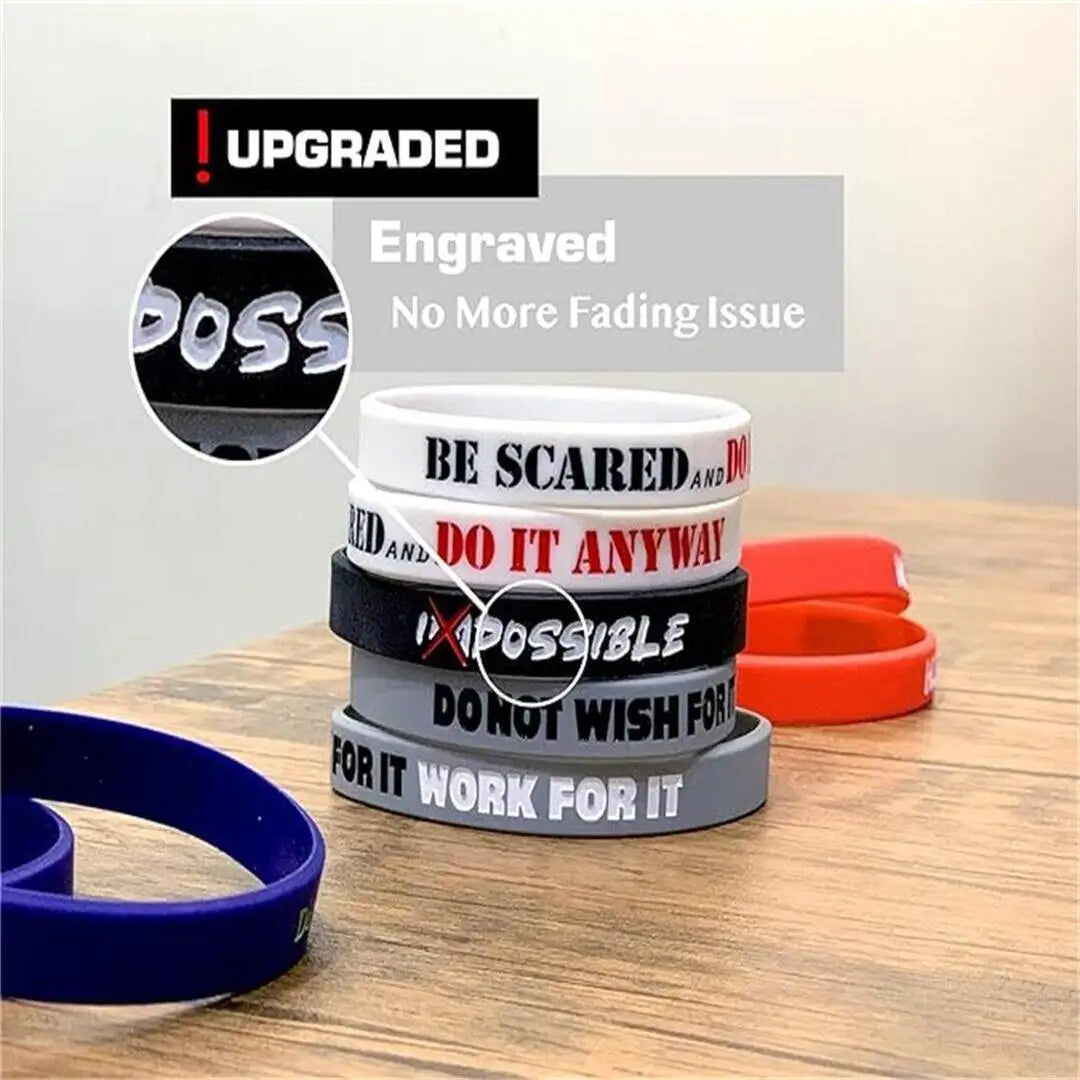 Pila de pulseras de silicona grabadas en negro, blanco y rojo con frases motivacionales como 'Be Scared' y 'Do It Anyway'