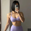 Una mujer vistiendo un sujetador deportivo de encaje morado con cordones y la parte inferior a juego, posando mientras se tom