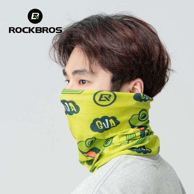 Eine Person trägt eine limettengrüne Gesichtsmaske mit schwarzem Logo und grünen Dinosaurier-Designs vor einem hellgrauen Hin