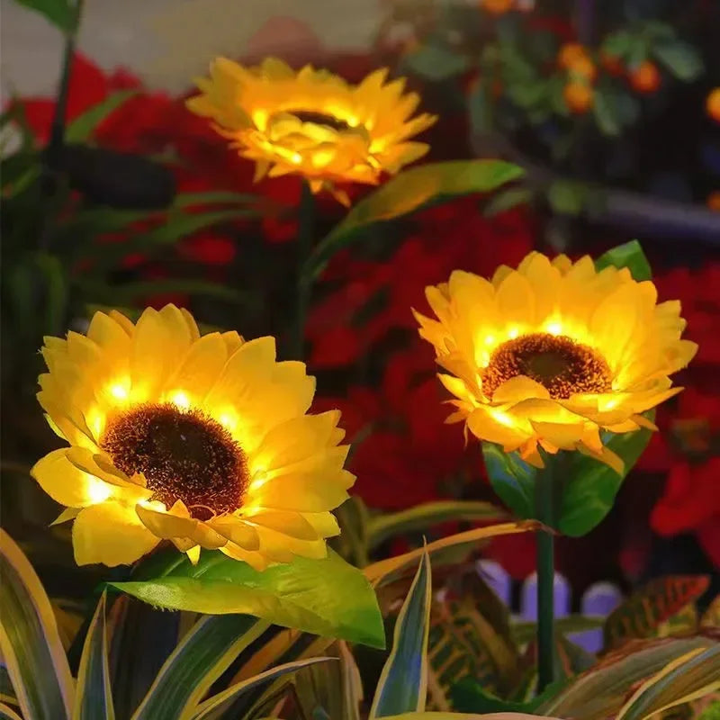 Three bright yellow solar sunflower LED stake lights blooming in a dark garden setting.