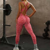 A woman wearing a red leopard print seamless yoga jumpsuit is posing in a gym setting.