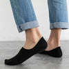 Une paire de chaussettes invisibles en silicone noires respirantes portées par une personne avec un jean bleu.