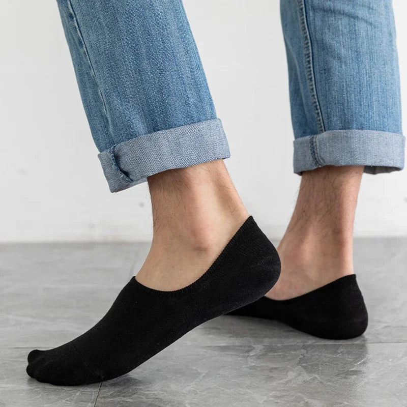 Une paire de chaussettes invisibles en silicone noires respirantes portées par une personne avec un jean bleu.