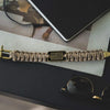 A tactical paracord survival bracelet with a bronze American flag charm resting on a dark surface.