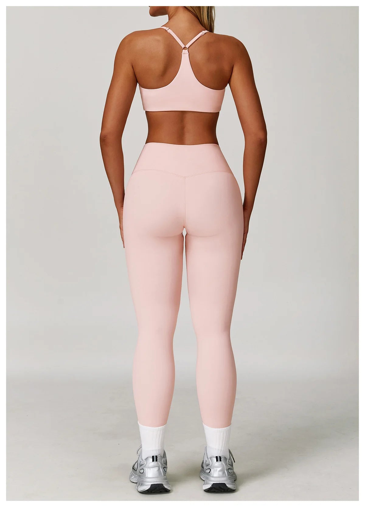 A woman models a pink three-piece yoga sports set consisting of a crop top, leggings, and sports bra.