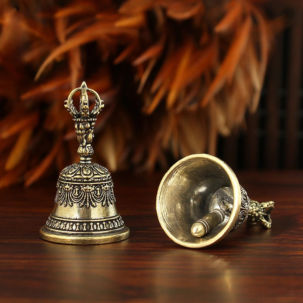Un tintement de cloche en bronze tenu à la main avec un dessus orné repose sur une surface en bois sombre.