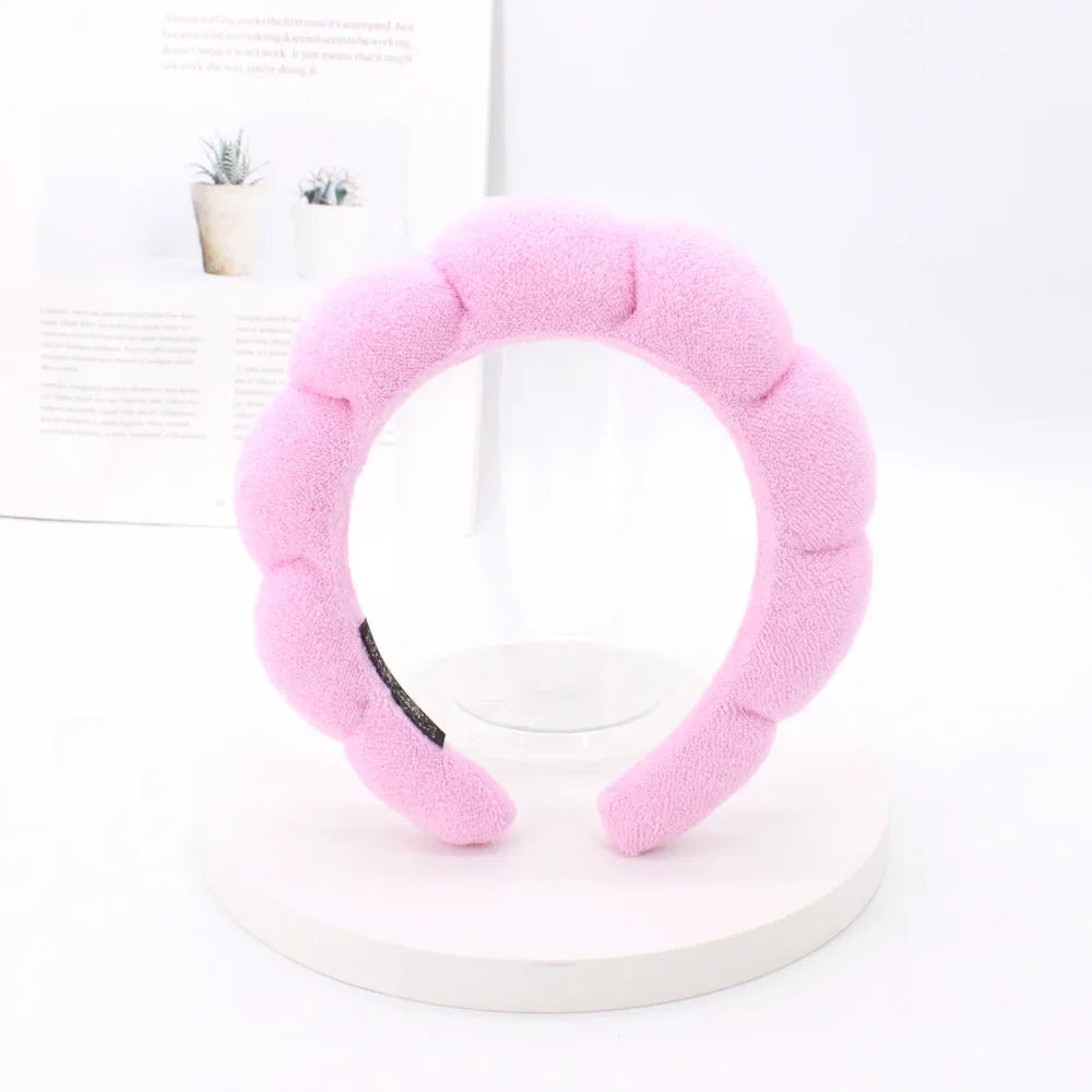 A pink sponge terry cloth headband for hair styling displayed on a white stand.