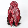 A deep red satin square scarf with white paisley and polka dot patterns tied around dark hair.