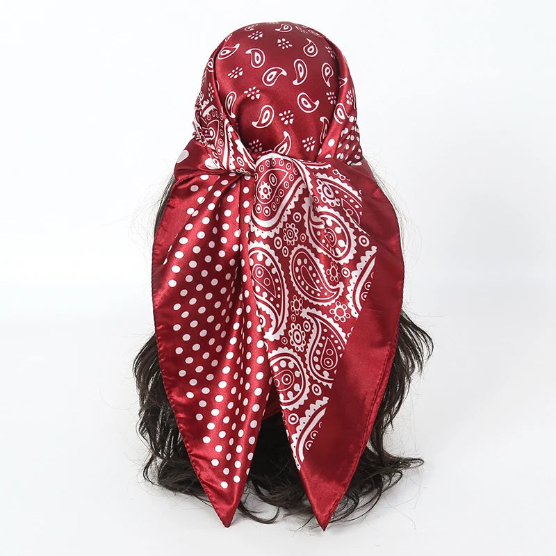 A deep red satin square scarf with white paisley and polka dot patterns tied around dark hair.