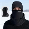 A man wearing a black double-layer winter beanie with a mesh face covering in a snowy outdoor setting.