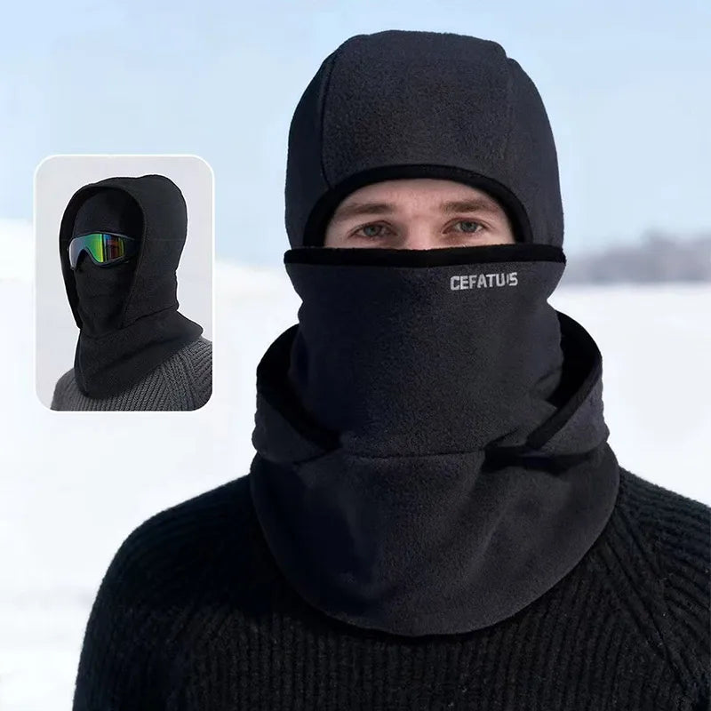 A man wearing a black double-layer winter beanie with a mesh face covering in a snowy outdoor setting.
