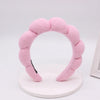 A pink sponge terry cloth headband for hair styling displayed on a white circular stand.