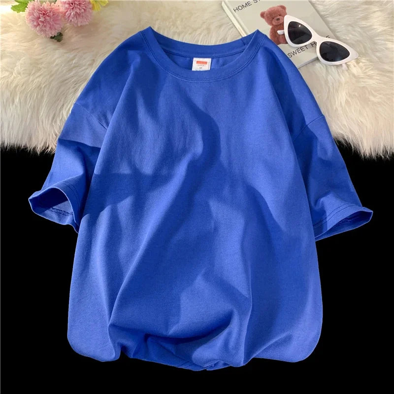 Ein königsblaues, oversized Baumwoll-T-Shirt für Damen liegt auf einer weißen flauschigen Oberfläche mit Sonnenbrille und Ted