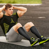 A muscular man wearing black athletic gear is sitting on a yoga mat outdoors.