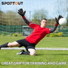 A male goalkeeper in a red shirt and black shorts is practicing catching a ball through a green net.