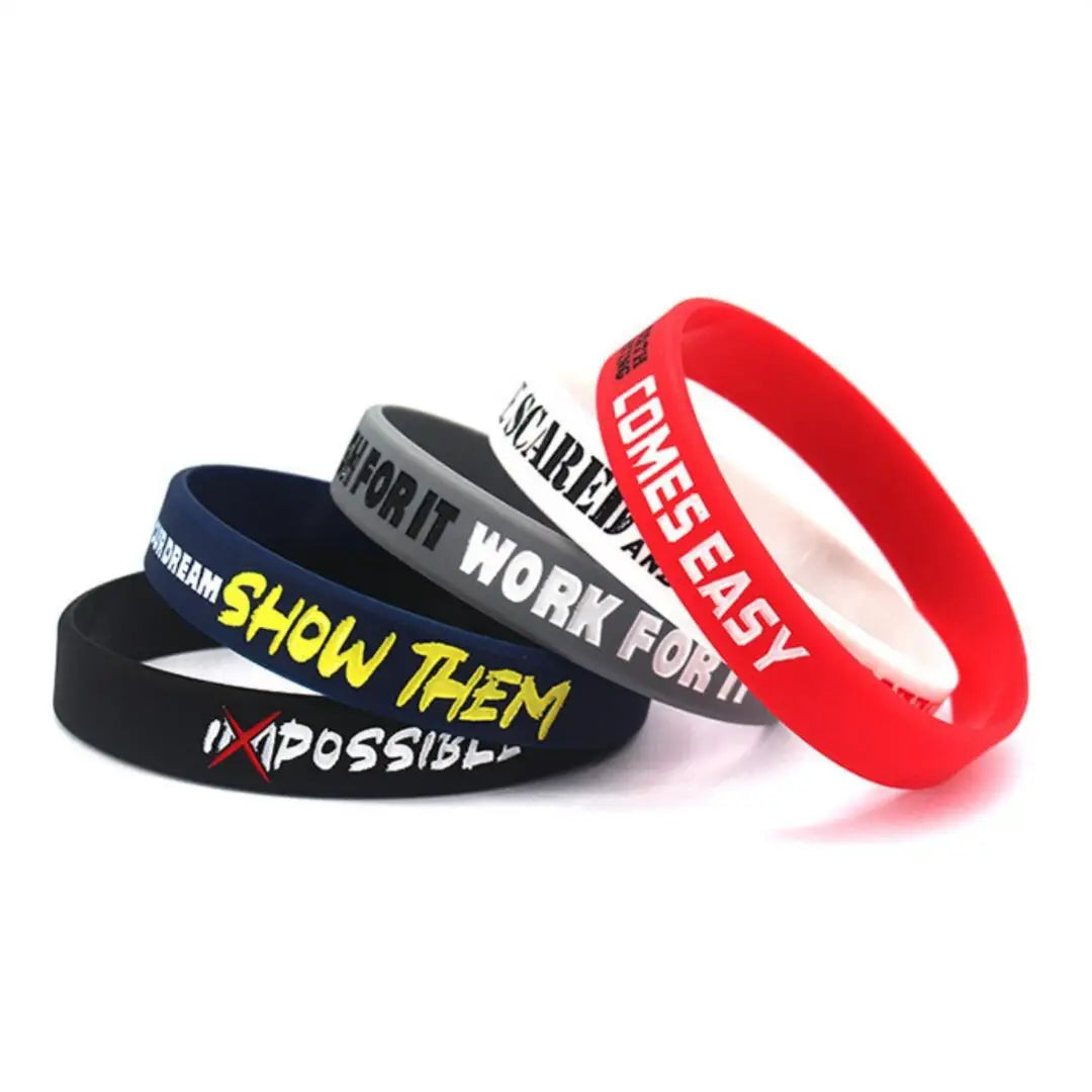 Tres pulseras de silicona en negro, gris y rojo con texto motivacional como 'Hazles imposible' y 'Sale fácil'.